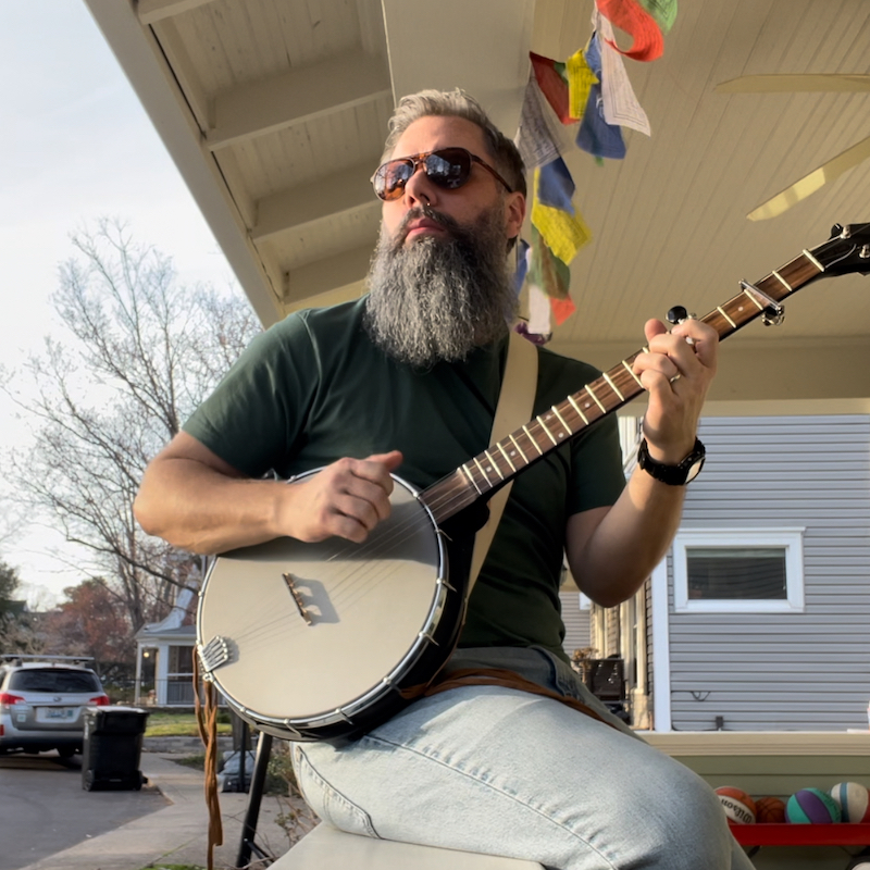 Barry wearing sunglasses and playing banjo sitting on a ledge.
